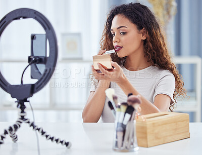 Hispanic female beauty blogger applying lipstick during a make-up tutorial while recording a video or doing a live for her blog with her smartphone