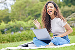 One young hispanic woman working on her laptop while sitting outside on an open field. A beautiful mixed race female student smiling while using her computer to study online on her university campus