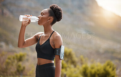 One young african american woman taking a break to drink some water while exercising outdoors. A beautiful and fit mixed race female athlete drinking from a bottle while working out in nature