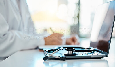 Closeup of a stethoscope lying on a laptop on a desk while a doctor writes a prescription in the background. Medical professional writing notes, planning with a laptop and stethoscope in the office