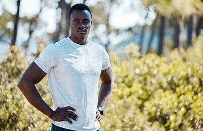 Young fit active african black male runner wearing sportswear and a watch standing with his hands on his hips looking serious and confident after a morning run outside in a forest. African male looking determined, thoughtful and resting after exercising i