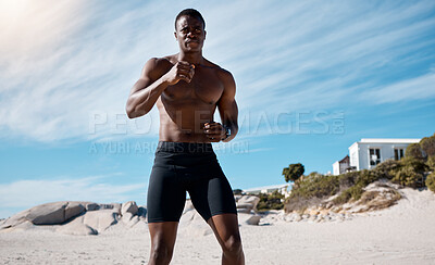 Buy stock photo A handsome young african american male athlete working out on the beach. Dedicated black man shadow boxing while exercising outside on the sand. Committed to a healthy lifestyle and getting fit