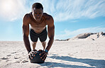 A handsome young african american male athlete working out on the beach. Dedicated black man exercising with a medicine ball outside on the sand. Committed to a healthy lifestyle and getting fit