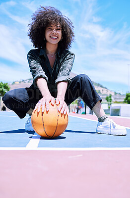 Cheerful young african african woman with curly afro squatting and holding a basketball on the court. Portrait of smiling woman about to play a game of basketball outside. Happy enjoying basketball