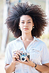 Young mixed race woman with curly hair taking creative photos on a vintage retro film camera. One female photographer looking in viewfinder while capturing pictures as a hobby or profession on a shoot