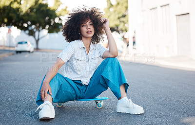 Buy stock photo A young female mixed race woman skate sitting on a skateboard looking cool and confident with great style in a street outside. Hispanic hipster woman with curly afro hair style in a cool outfit against a urban background