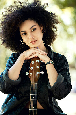 Happy young smiling mixed race female musician enjoying playing her guitar in the park in nature alone. Young hispanic woman with a curly afro relaxing while playing the guitar outside on a field