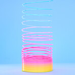 Closeup of a colourful flexible plastic rainbow slinky toy in stretched out motion isolated against a blue background. Entertaining childhood color item for playing, fun and games. Spirals leading in a upward direction