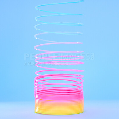 Buy stock photo Rainbow slinky toy, spring and plastic product in studio isolated against a blue background mockup. Flexible toys, colorful spirals and childhood item stretched out for playing, having fun and games.