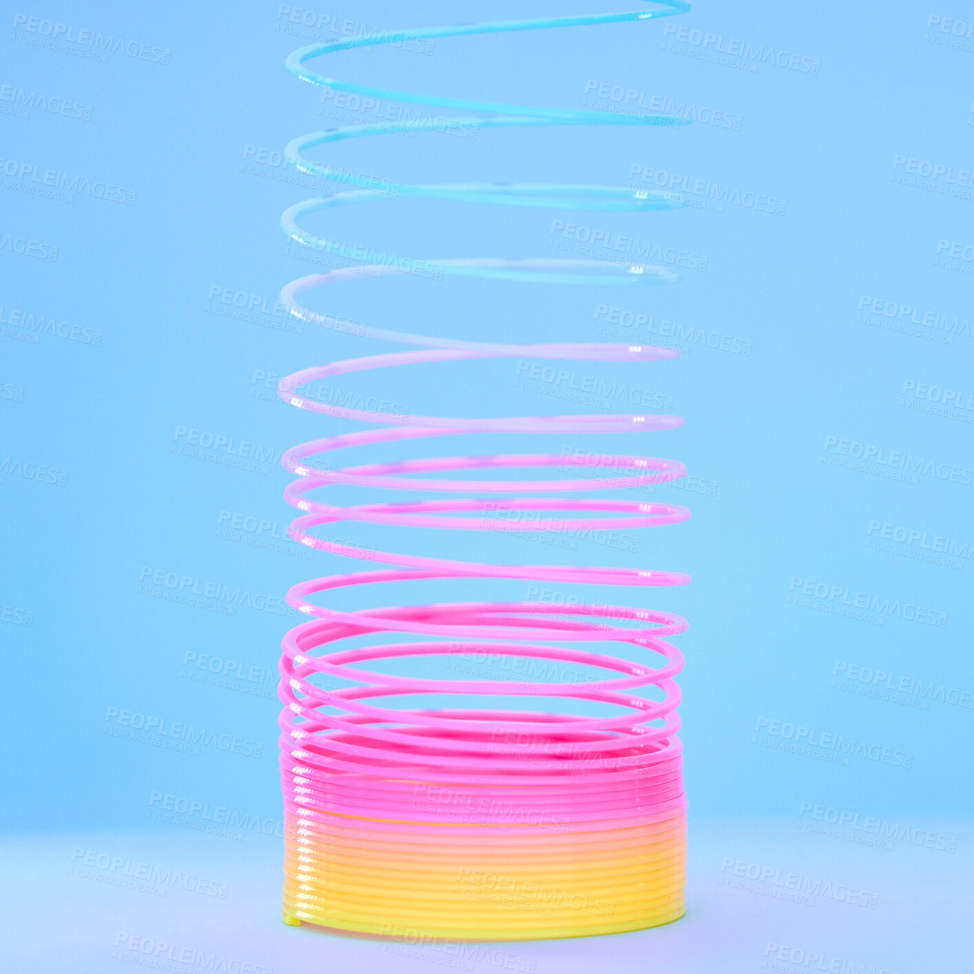 Buy stock photo Rainbow slinky toy, spring and plastic product in studio isolated against a blue background mockup. Flexible toys, colorful spirals and childhood item stretched out for playing, having fun and games.