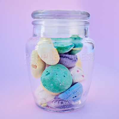A closeup of a glass jar filled with a variety of colourful painted little beach stones isolated against a purple background. A good little concept of interior decoration and gives a feeling on summer time