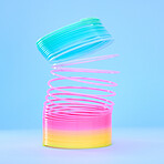 Closeup of a colourful flexible plastic rainbow slinky toy in stretched out motion isolated against a blue background. Entertaining childhood color item for playing, fun and games. Spirals leading in a upward direction