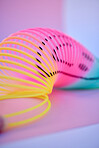 A brightly coloured neon slinky isolated against a multicoloured background in studio. A fun and imagination inspiring toy for kids of all ages. Brilliant colours producing positive feelings and vibes