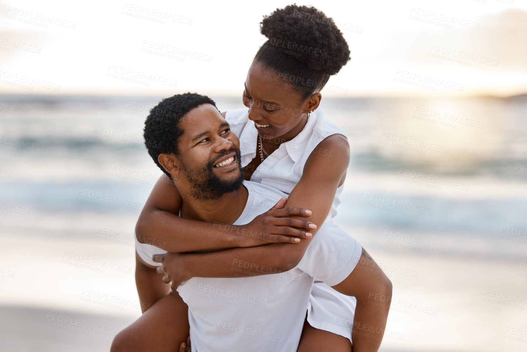 Buy stock photo Young happy african American couple spending a day at the sea together. Cheerful boyfriend giving his girlfriend a piggyback on the beach. Caring husband and wife bonding on the seashore