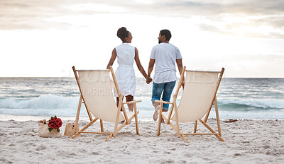 Buy stock photo Rearview of a cheerful african american couple spending a day at the sea together. Happy boyfriend and girlfriend holding hands while walking on the beach. Caring husband and wife bonding on the seashore