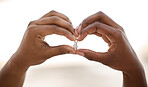 Closeup of the hands on an african american man making a heart shape while holding a ring. Man making a heart gesture with his hands while showing a ring on a beach