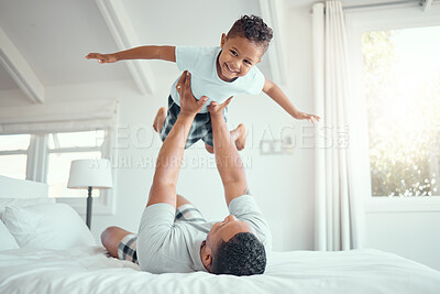 Buy stock photo Cute little mixed race boy lying in fathers arms while looking at the camera and smiling. Loving family with father lifting happy little child son playing plane and having fun on bed