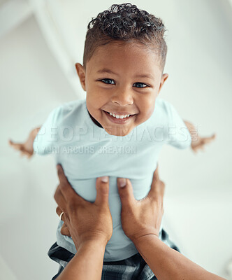 Buy stock photo Happy little mixed race boy lying in fathers arms while looking at the camera and smiling. Loving family with father lifting cute little child son playing plane and having fun while bonding at home