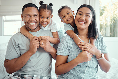 Buy stock photo Portrait of a happy young mixed race family with two children wearing pyjamas and sitting at home together. Cute little girl and boy embracing their mother and father from behind