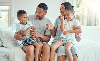 Happy funny mixed race family with two children wearing pyjamas and sitting together at home. Cheerful parents sitting in their bedroom with their daughter and son laughing and having fun in the morning