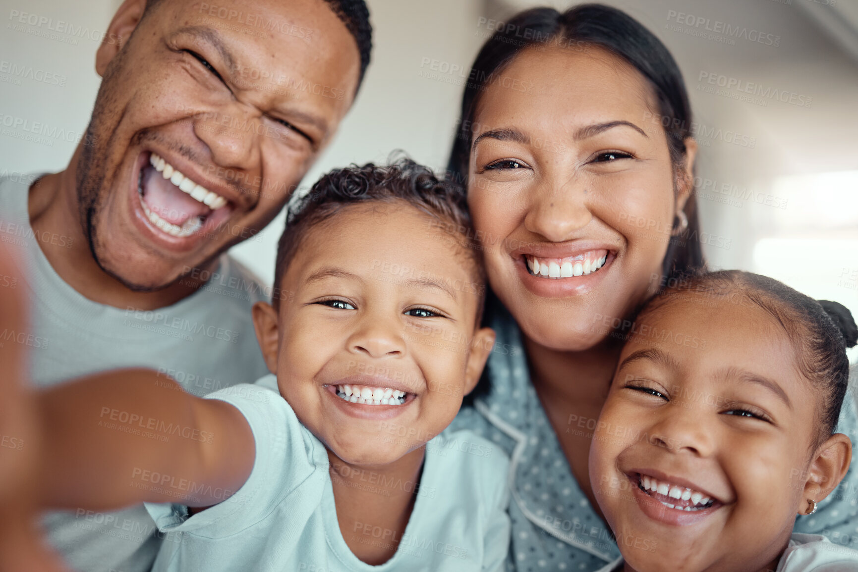 Buy stock photo Cute little boy holding phone and taking selfie or recording funny video with his family. Happy mixed race family with two children and parents posing together for a family picture on a mobile phone