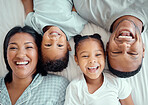 Portrait of happy funny mixed race family with two children relaxing and lying together on a bed at home, from above. Faces of little brother and sister spending time with their loving parents