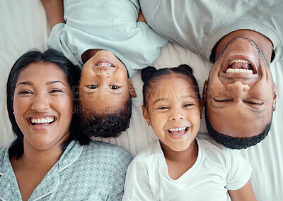 Buy stock photo Portrait of happy funny mixed race family with two children relaxing and lying together on a bed at home, from above. Faces of little brother and sister spending time with their loving parents