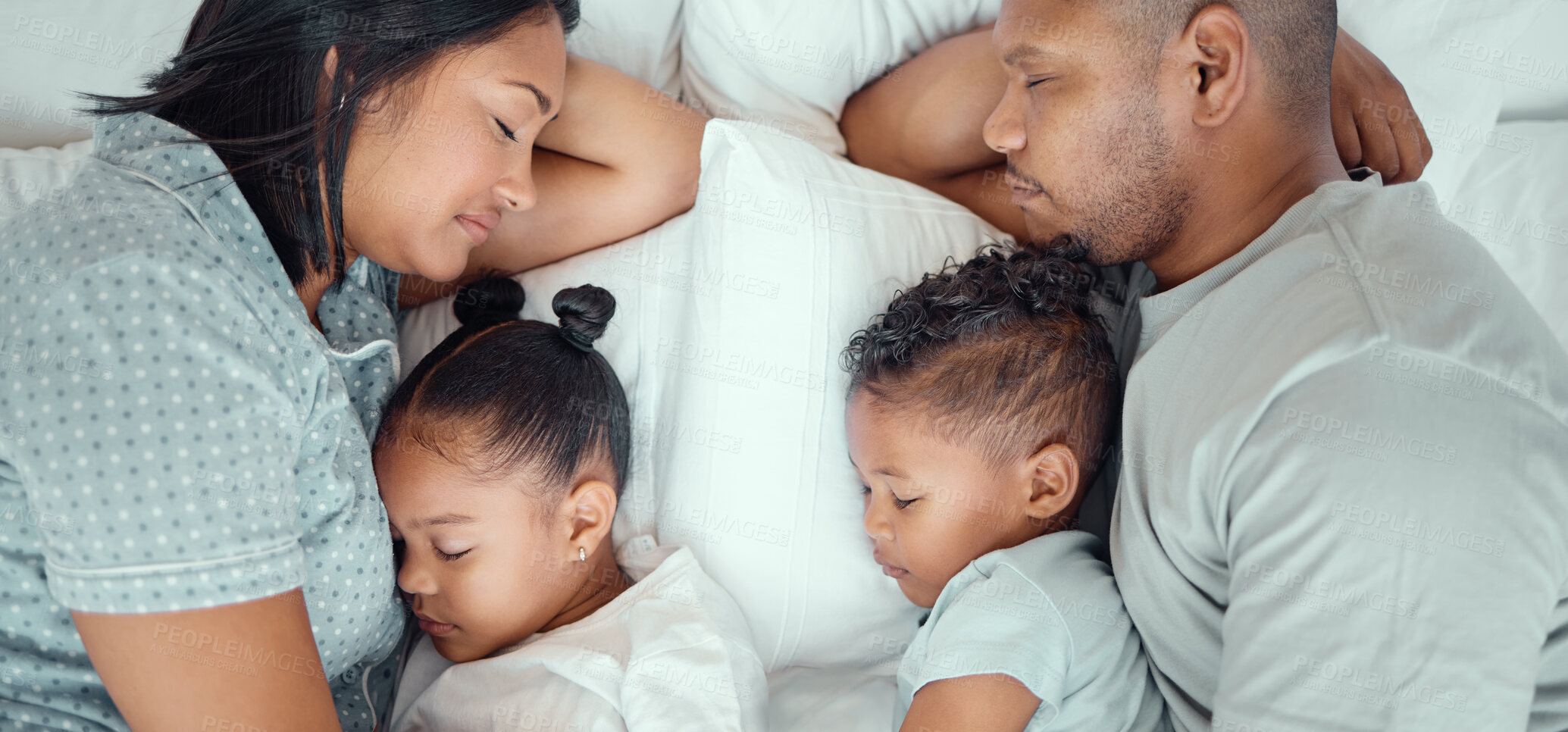 Buy stock photo Happy family with two children sleeping together in their parents bed, from above. Loving parents cuddling two little kids for bedtime. Adorable girl and boy taking a nap and rest with mom and dad