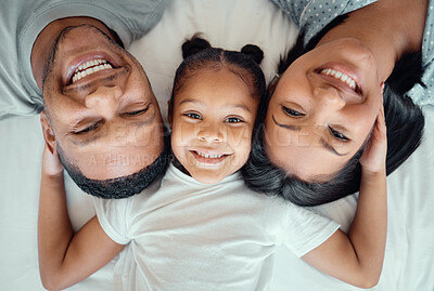 Adorable little girl pulling her parents close while lying in between her mother and father, from above. Faces of loving parents bonding with their daughter lying on a bed and spending free time together on the weekend