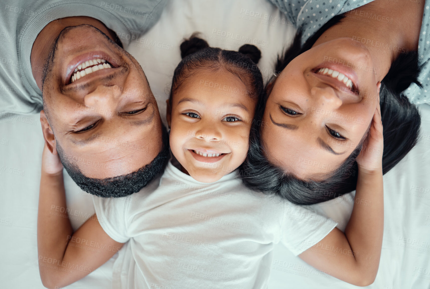 Buy stock photo Adorable little girl pulling her parents close while lying in between her mother and father, from above. Faces of loving parents bonding with their daughter lying on a bed and spending free time together on the weekend