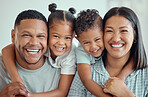 Portrait of a happy young mixed race family with two children wearing pyjamas and sitting at home together. Cute little girl and boy embracing their mother and father from behind