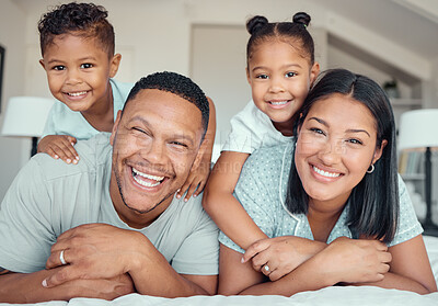 Portrait of a cheerful family lying together on bed. Little boy and girl lying on their parents laughing and having fun. Mixed race couple bonding with their son and daughter. Hispanic siblings enjoying free time with their mother and father