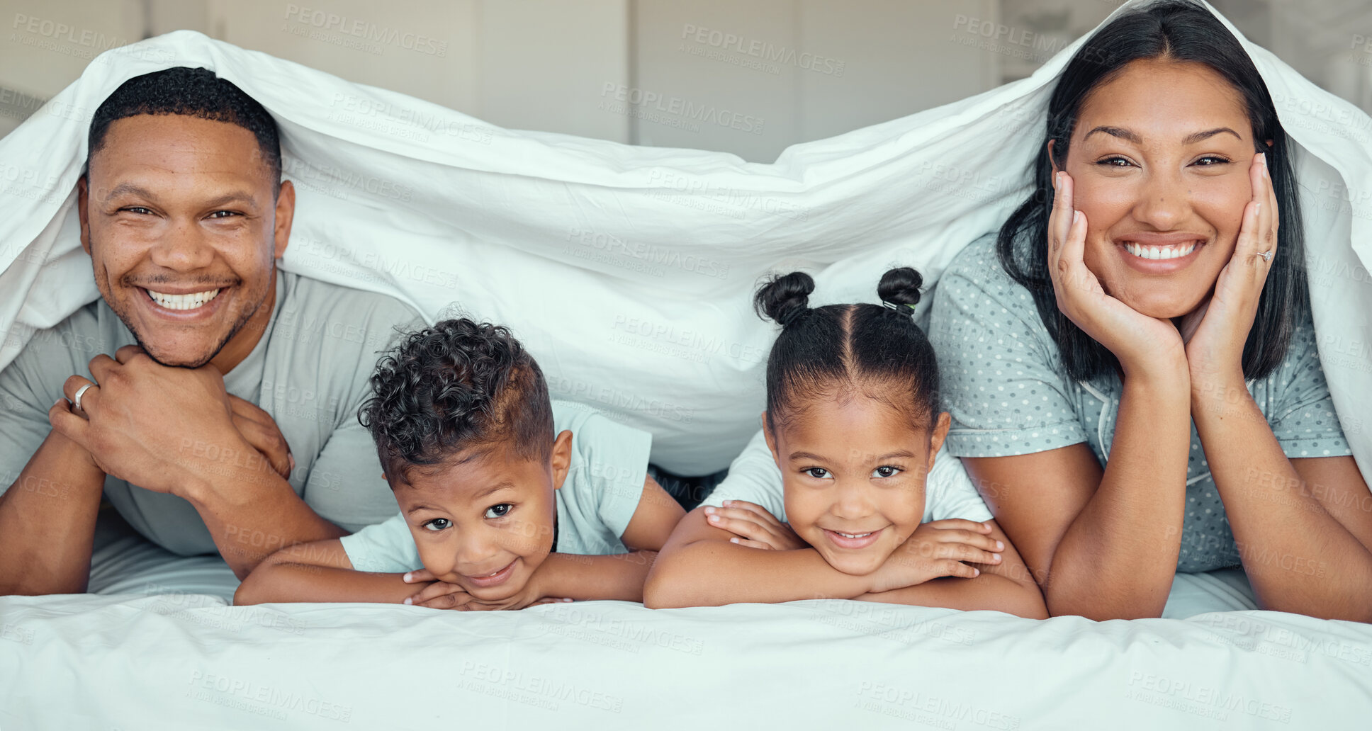 Buy stock photo Portrait of happy family with two children lying under duvet smiling and looking at camera. Little girl and boy lying in bed with their parents bonding and having fun