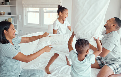 Buy stock photo Two happy children laughing and enjoying pillow fight with parents in bedroom at home. Joyful kids daughter and son playing with mother and father. Fun mixed race family spending time together at home in the morning