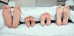 Feet of family lying in bed. Close up of feet of parents and two children in bed. Family relaxing in bed together. Below bare feet of family sleeping in bed. Kids resting in bed with their parents