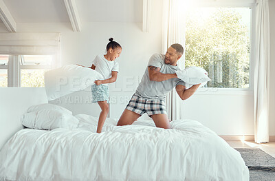 Buy stock photo Adorable little girl laughing and enjoying fun pillow fight with dad on a bed in the morning. Cheerful father and daughter in pyjamas bonding and spending time together at home