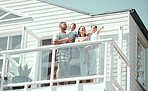 Happy mixed race family with two children wearing pyjamas while standing on balcony at their new house or while on holiday. Adorable little girl pointing at sky and showing family something outside