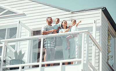 Buy stock photo Happy mixed race family with two children wearing pyjamas while standing on balcony at their new house or while on holiday. Adorable little girl pointing at sky and showing family something outside