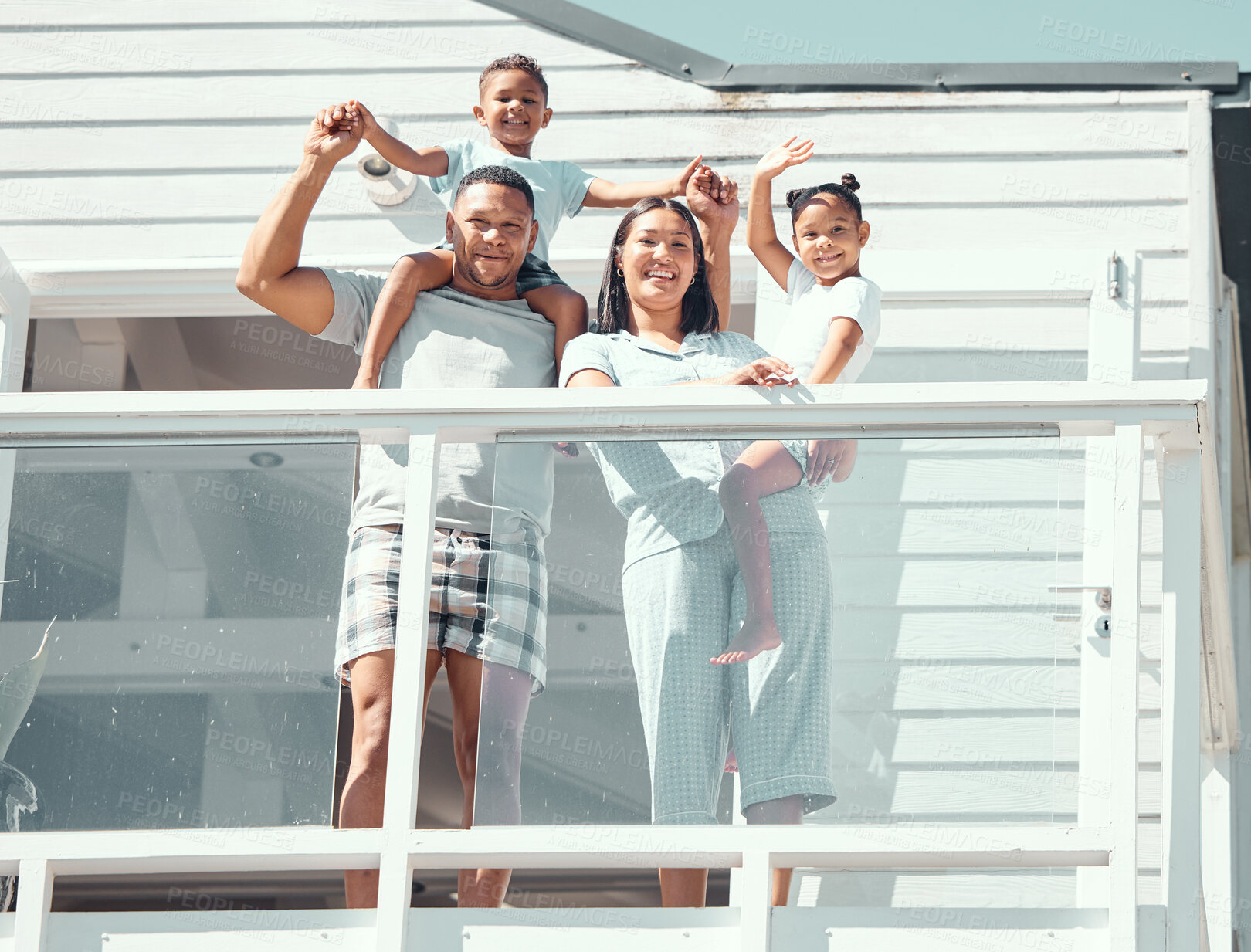 Buy stock photo Portrait of happy mixed race family with two children wearing pyjamas and smiling and waving at camera while standing on balcony at their new house or while on holiday