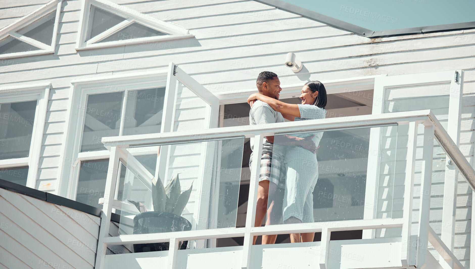Buy stock photo Loving young mixed race couple in pyjamas sharing romantic moment while dancing on the balcony of their new home or while on holiday enjoying their honeymoon