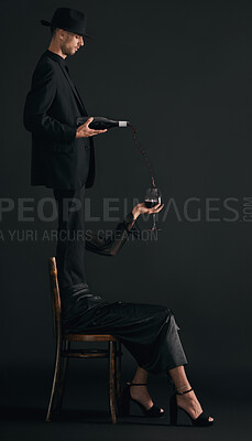 One handsome young man dressed smartly pouring red wine into the glass of an unrecognizable woman in studio isolated against a black background. Concept shot of a female wine tasting in black attire