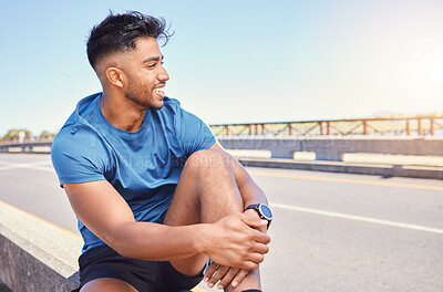 Happy smiling young mixed race fit man enjoying a break from exercising outside. Hispanic male sitting down before starting his cardio workout outdoors. Positive and his fitness and heart health