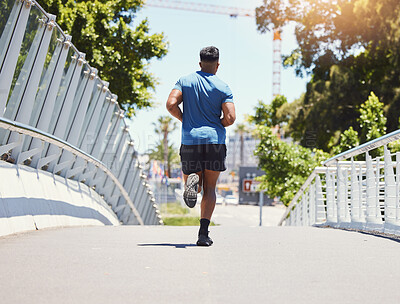 Buy stock photo Rearview fit athletic mixed race man running across a bridge in the city for fitness. Young hispanic male outdoors for a cardio workout during the day. Dedicated to fitness and a healthy lifestyle
