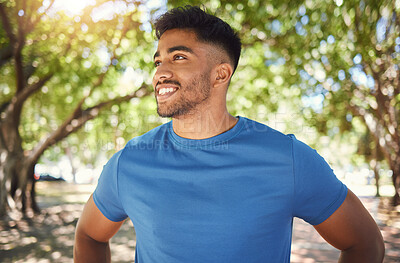 Happy young mixed race fit man enjoying a break from exercising outside in a park. Hispanic male standing with his hands on his hips during a cardio workout. Looking away and thinking about fitness