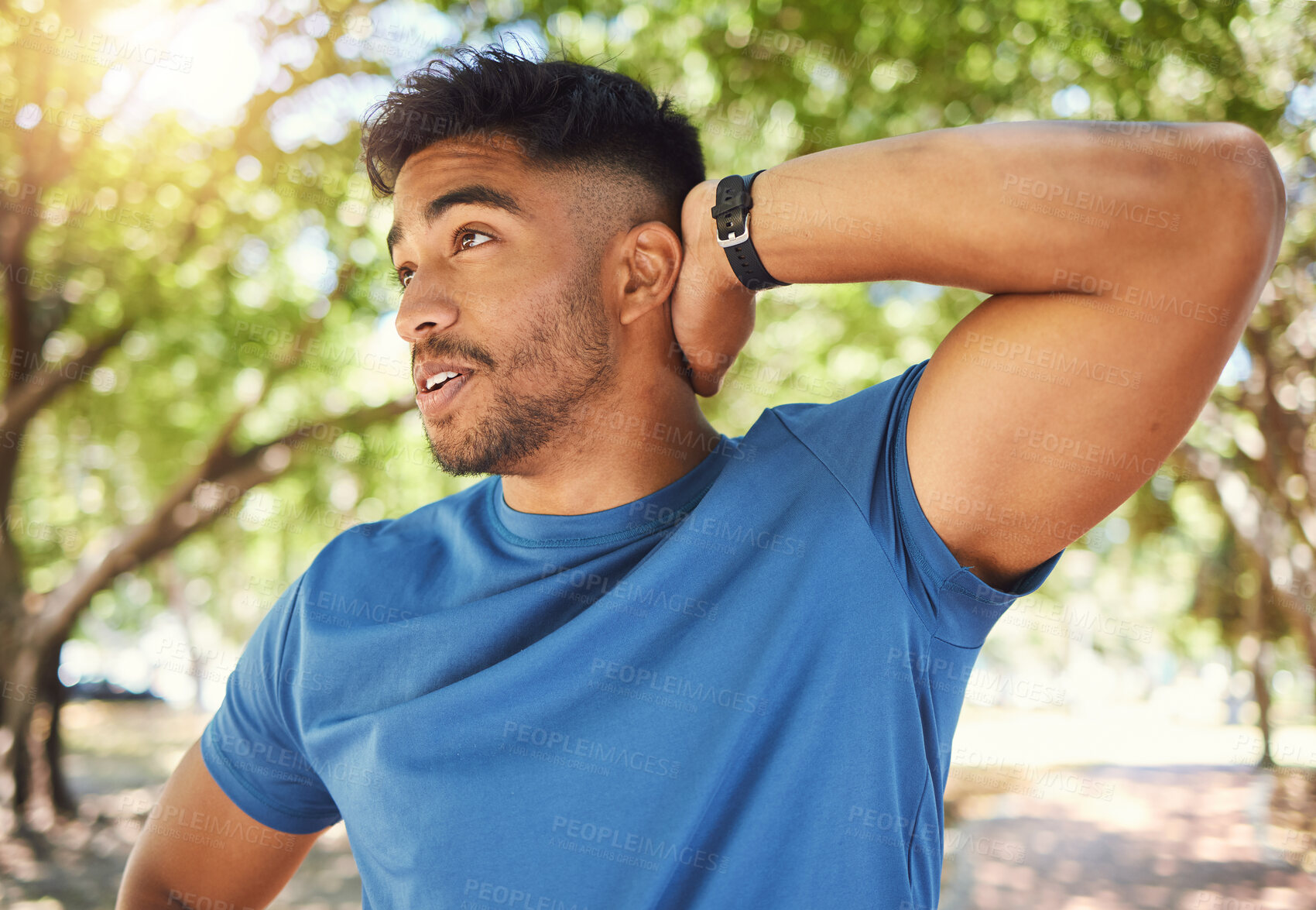 Buy stock photo Fit athletic man smiling while stretching his arms during a workout at the park. Hispanic man doing warm-up exercises outdoors on a sunny day. Athletic man taking a break from a fitness routine 