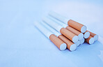 Closeup of a pack of cigarettes isolated on a blue background. Macro view of a group of tobacco cigarettes stacked together and lying down. Smoking addiction is unhealthy and harmful to wellbeing 