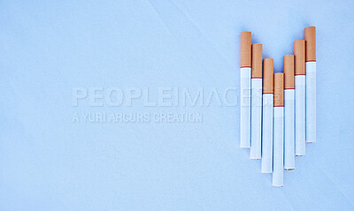 Studio shot of cigarettes in a line shaped like an arrow or arrow pointing down isolated against a blue background. Tobacco and nicotine are addictive and harmful and will cause your health to decline