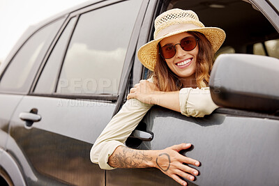 Buy stock photo One beautiful caucasian woman hanging out the window of a car while taking a roadtrip. Attractive young female hipster with tattoos on her arm, wearing a hat and sunglasses and taking a drive in a car