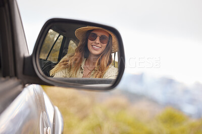Buy stock photo Reflection in the rear view mirror of a young beautiful woman's car while travelling to a vacation on a sunny day. Caucasian woman wearing sunglasses and a hat inside a car going on a roadtrip looking at her reflection and smiling while driving on the road 
