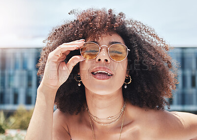 Young mixed race woman with curly natural afro hair wearing trendy and stylish sunglasses outside. One female only looking carefree, cool and confident. Happy fashionable hispanic woman in the city